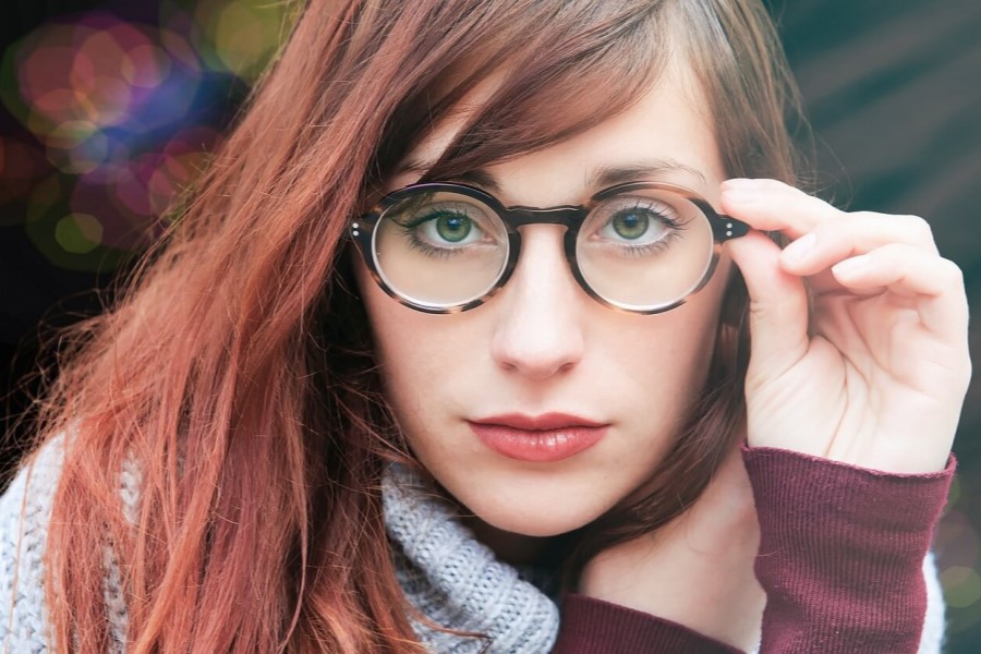 Młoda kobieta w okularach korekcyjnych spogląda w stronę obiektywu.